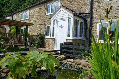 a house with a white door and a pond at Brocken Brae Cottage in Easby