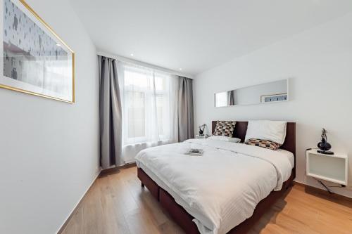 a white bedroom with a large bed and a window at Surreal cocoon in Brussels center in Mellet