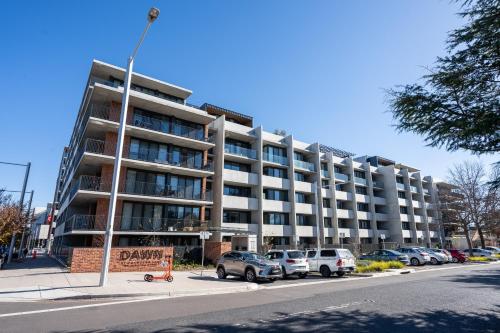 a large apartment building with cars parked in a parking lot at Rooftop patio w Mt View, Parking, Wifi n Netflix in Braddon