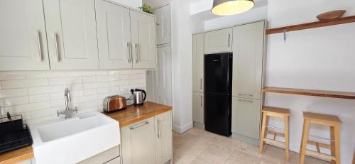 a kitchen with white cabinets and a black refrigerator at Double Bed at Cozy Hailsham in London