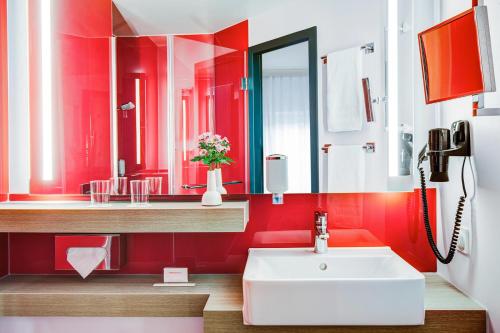 Baño rojo con lavabo y espejo en IntercityHotel Rostock, en Rostock