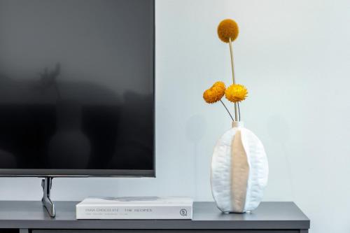 a white vase with yellow flowers in it next to a tv at Rooftop patio w Mt View, Parking, Wifi n Netflix in Braddon