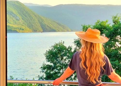 a woman sitting on a balcony looking out at a lake at Vikendica Dijana Ramsko jezero 