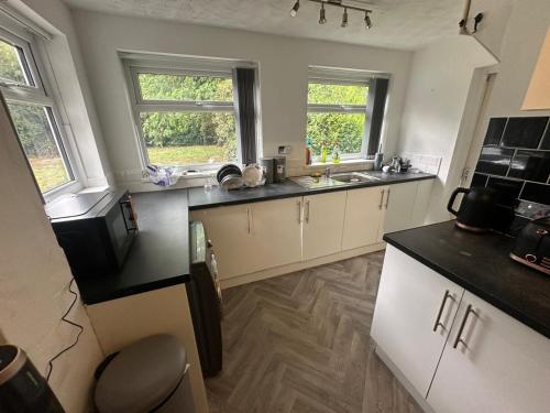 a kitchen with white cabinets and a sink and two windows at Ashdene hideaway in Bickenhill