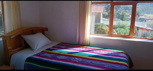 a bedroom with a bed with a colorful blanket and a window at Misky Wasi Lodge De Gloria Amantani lsland Occosuyo community in Puno