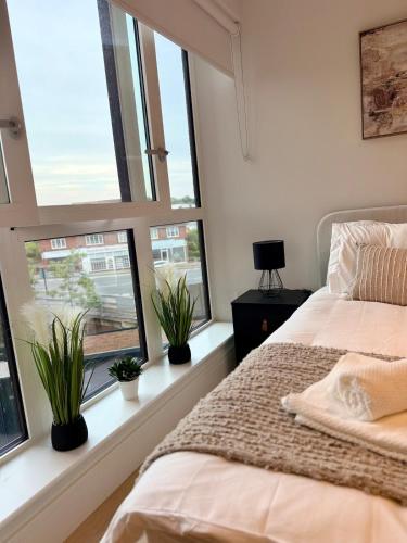 a bedroom with windows and a bed with plants at Luxury 2bed With Gym Cinema & Games Room in New Malden