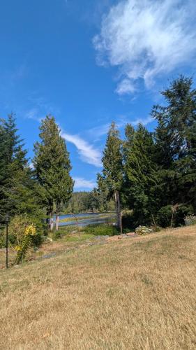 a field of grass with trees and a body of water at Davidson Star in Sooke