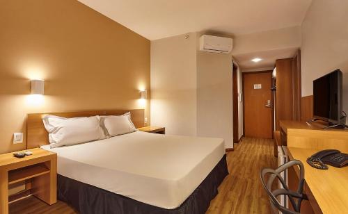 a hotel room with a large white bed and a desk at Hotel Nacional Inn Bauru in Bauru