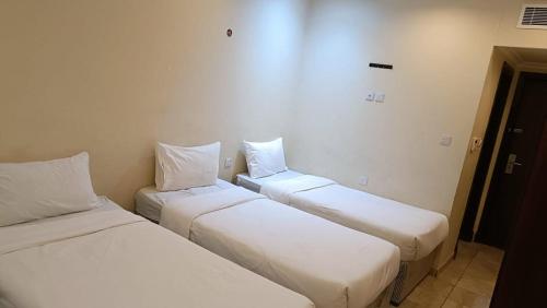 3 camas en una habitación con sábanas y almohadas blancas en فندق البركة, en Al Hindāwīyah