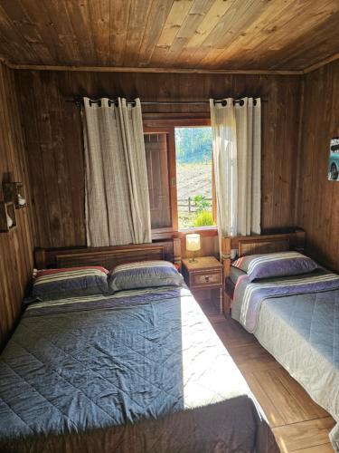 two beds in a wooden room with a window at Chalé in Itati