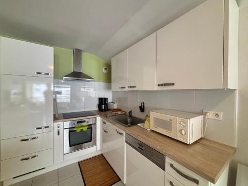 une cuisine avec des armoires blanches, un évier et un micro-ondes dans l'établissement Appartement central avec garage à 2 min de la plage, balcon, wifi, proche commerces - FR-1-197-188, à Les Sables-dʼOlonne