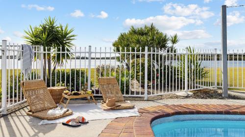 a fence with two chairs next to a swimming pool at Peninsula Court Unit 9 - Absolute Waterfront Escape - Holiday Yamba in Yamba