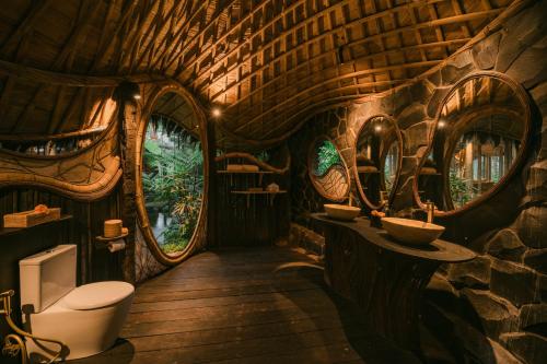 a bathroom in a tree house with a toilet and mirrors at Hideout Eco Bamboo House Bali in Selat