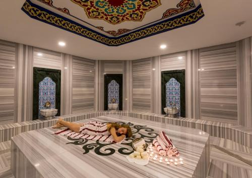 a woman laying on a bed in a room with windows at Side Royal Palace in Side