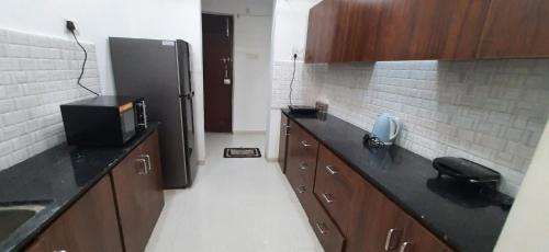a kitchen with a black refrigerator and wooden cabinets at Staeg Night Sky View 2BHK - 1605 in Indore