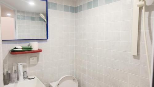 a white tiled bathroom with a toilet and a mirror at FFC sweet home on Shaanxi Road in Shanghai
