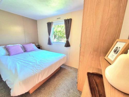 a bedroom with a bed with purple pillows and a window at Cherry, 2 Bed, 6 Berth With Electric Panel Heaters 70724C in Great Yarmouth