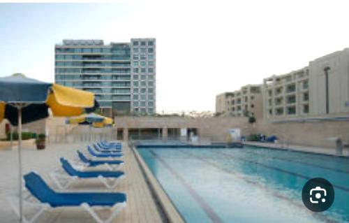 a swimming pool with chairs and umbrellas next to a building at אוקיינוס במרינה הרצליה פיתוח in Herzliyya B