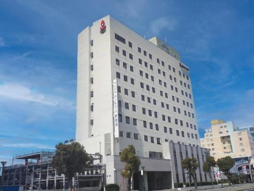 a tall white building with a red symbol on it at Hotel Route-Inn Niihama in Niihama
