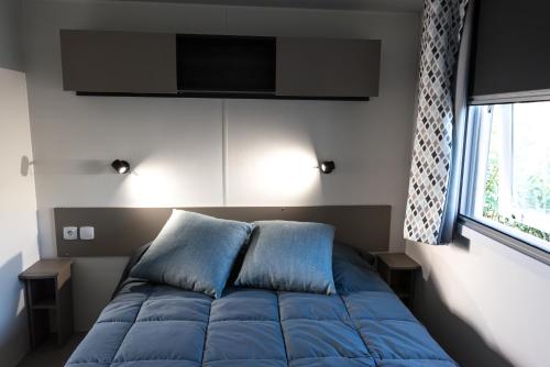a bed with blue pillows in a room with a window at Mobile home confort - Fréjus - camping 4 étoiles - in Fréjus