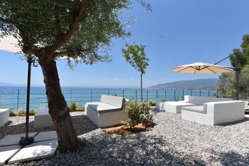 Un patio con sofás blancos y una sombrilla y el océano. en Potis Suites, en Almirón