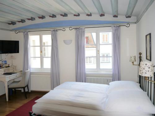 a bedroom with a bed and a desk and windows at Hotel Obertor in Ravensburg