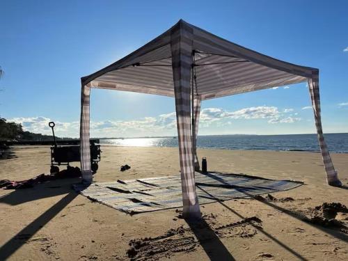 a tent on a beach with the ocean at Pantai Indah Cottage in Hervey Bay