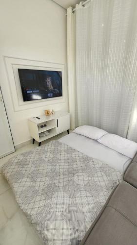 a white bedroom with a bed and a tv at Flat Esmeralda Juquehy in São Sebastião