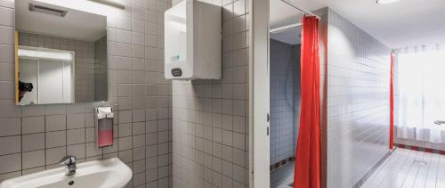 a bathroom with a sink and a red shower curtain at HI Youth Hostel Lindau in Lindau