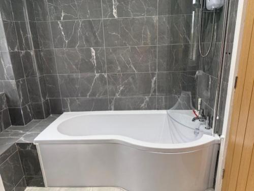 a white bath tub in a bathroom with black tiles at Stylish 4 bed in Central Conwy in Conwy