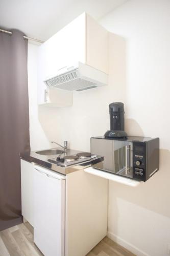 Il comprend une petite cuisine blanche avec un four micro-ondes et un évier. dans l'établissement Charming and cozy Near Montparnasse, à Paris
