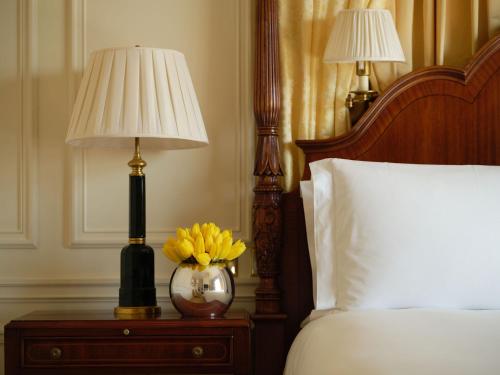 a bed with a lamp and a vase of yellow flowers on a table at The Savoy in London