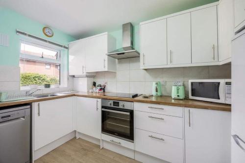 a white kitchen with white cabinets and a microwave at Sea Cloud - 2-bedroom House with Courtyard Garden in Poole