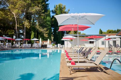 a row of lounge chairs with umbrellas and a swimming pool at Hotel Pelegrin Plava Laguna in Umag