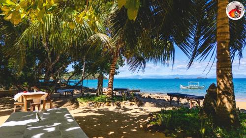 a beach with tables and palm trees and the ocean at Djema Forest in Nosy Be