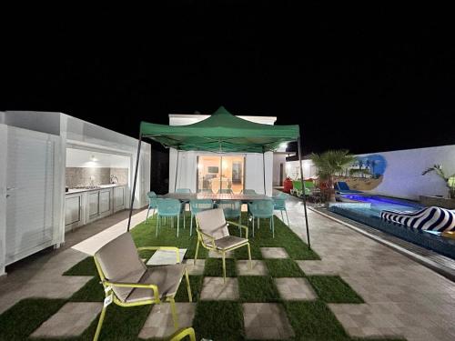 a patio with a table and chairs and a green umbrella at Villa SUN SQUARE DJERBA in Awlād ‘Umar