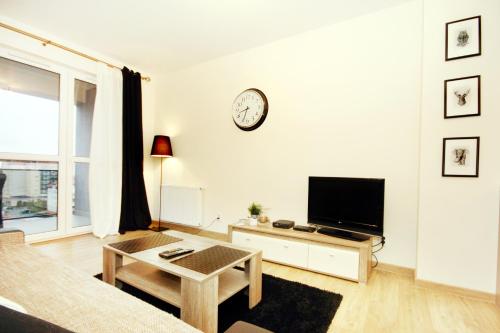 a white living room with a tv and a clock on the wall at Livin Apartments Santocka in Szczecin
