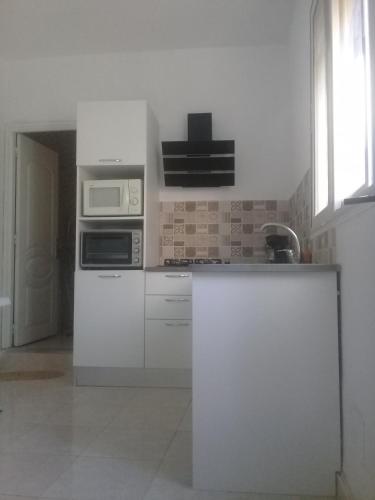a white kitchen with a microwave and a sink at maison de charme au cœur du foret et plage de la grotte Bizerte in Banzart