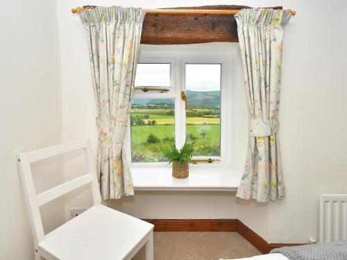 una finestra con tende e una sedia in una stanza di Osprey Cottage a Bassenthwaite