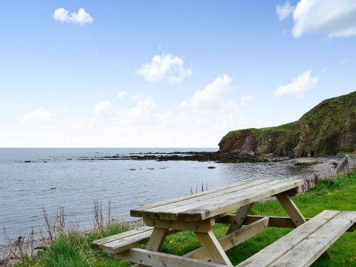 a wooden picnic table sitting on the grass near the water at Archie's Cottage in Burnmouth