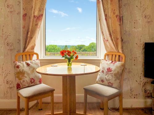 une table et deux chaises avec un vase de fleurs dans une fenêtre dans l'établissement Old Barn Farm Cottage - Cc, à Uplawmoor