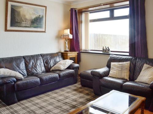 a living room with a leather couch and a table at Old Stable Cottage in Uplawmoor