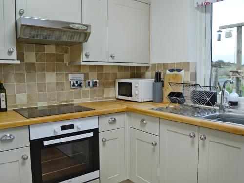 a kitchen with white cabinets and a sink and a microwave at Kirklauchline Cottage in Portpatrick