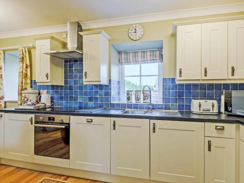 a kitchen with white cabinets and a clock on the wall at Bwthyn - Uk31387 in Caeathro