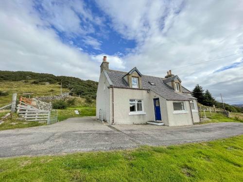 a small white house with a blue door on a road at Dalcharn in Bettyhill
