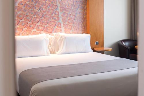a bedroom with a bed with white pillows and a wall at Abba Sants in Barcelona
