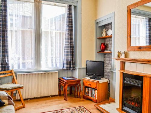 a living room with a television and a fireplace at Kirk Wynd Cottage in Kirriemuir