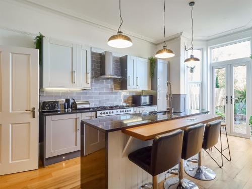 a kitchen with white cabinets and a island with bar stools at Belmont House in Broadstairs