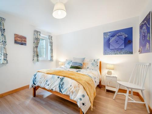 a bedroom with a bed and a white chair at Postbox Cottage in Catacol