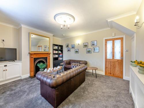 a living room with a leather couch and a fireplace at Lundy Cottage in Alnwick